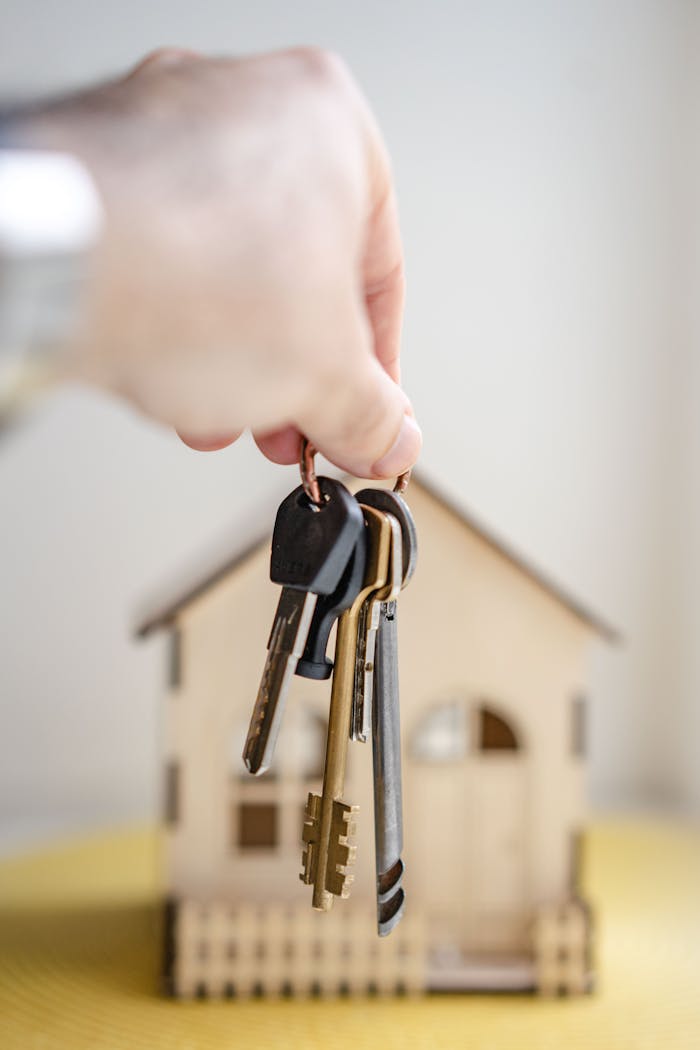 services-03 Crop faceless real estate agent with keys from new house bought with mortgage against wooden model of building