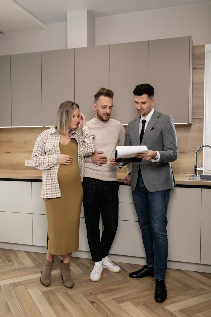 gallery-4 Young couple discusses real estate options with realtor in modern kitchen setting.