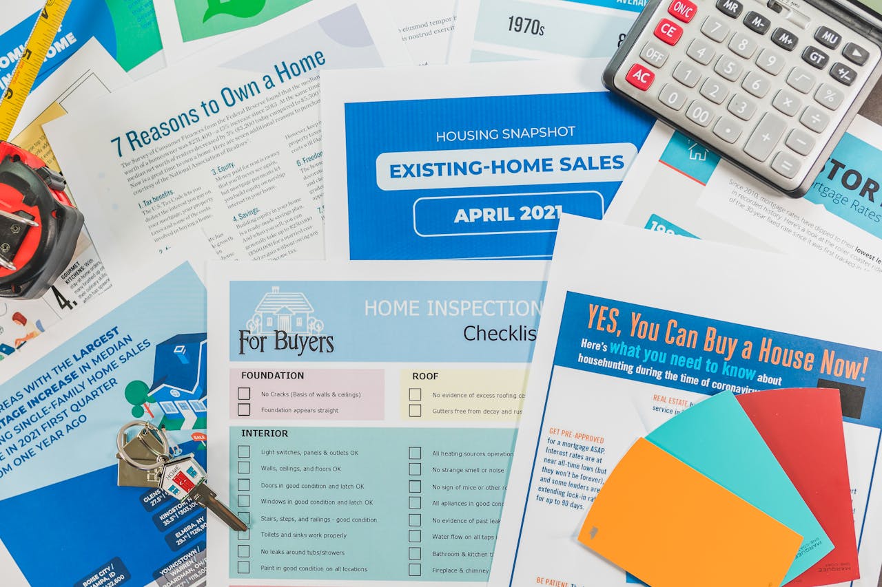 gallery-1 Flat lay of real estate brochures, checklists, and a calculator for home buying.